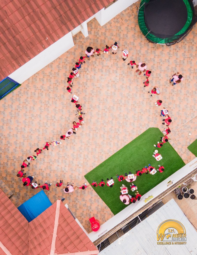 Students forming a long hand-in-hand chain across the school courtyard, seen from above